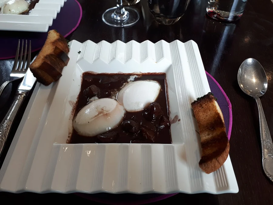 Deux œufs en meurette nappés de sauce au vin rouge, servis avec des croûtons dans une assiette carrée