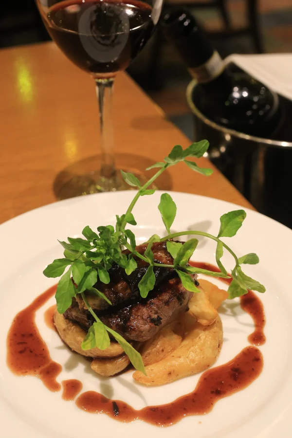 Un tournedos de bœuf servi sur des pommes de terre avec une sauce au vin rouge, dans une assiette blanche