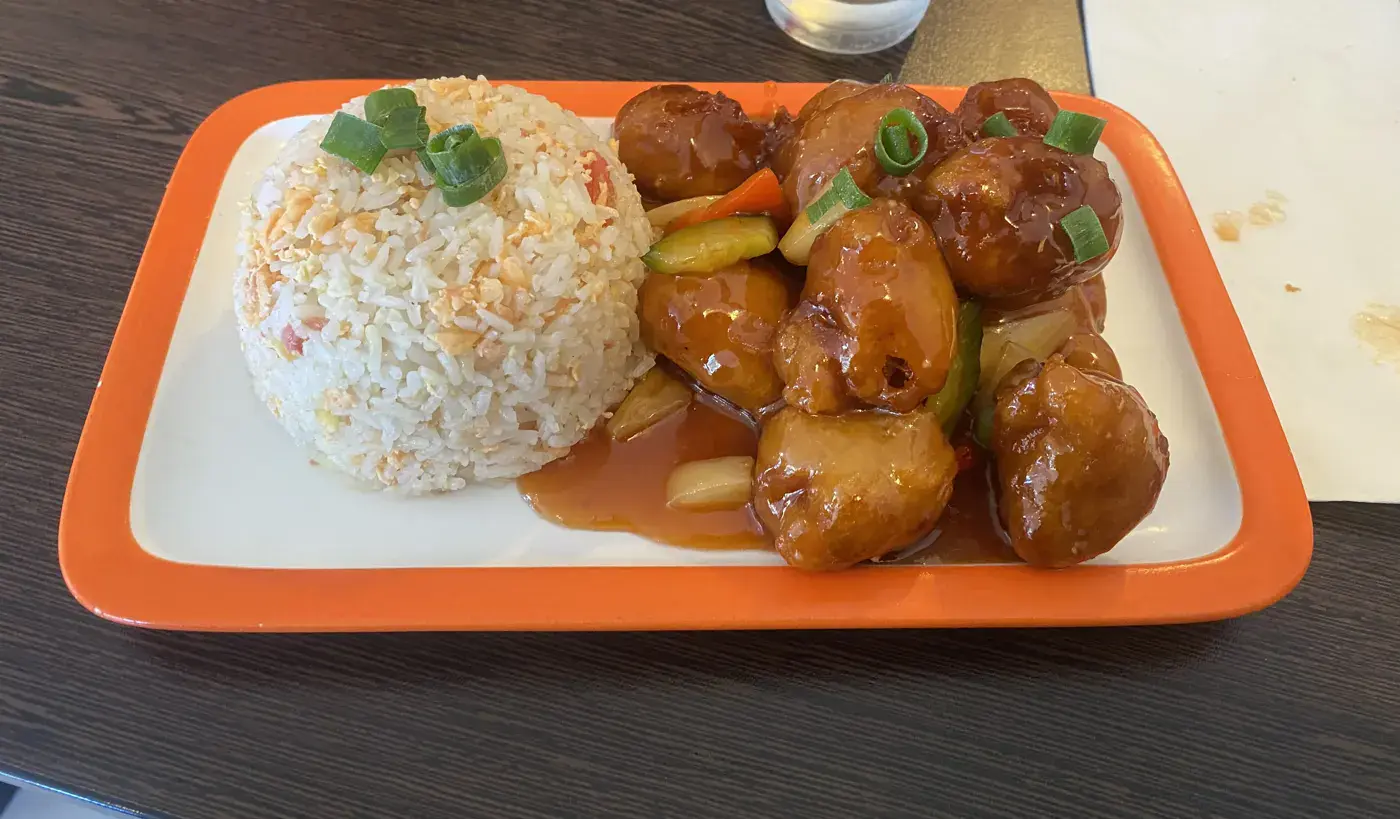 Assiette de porc aigre-doux nappé de sauce avec légumes sautés, servi à côté d’un dôme de riz