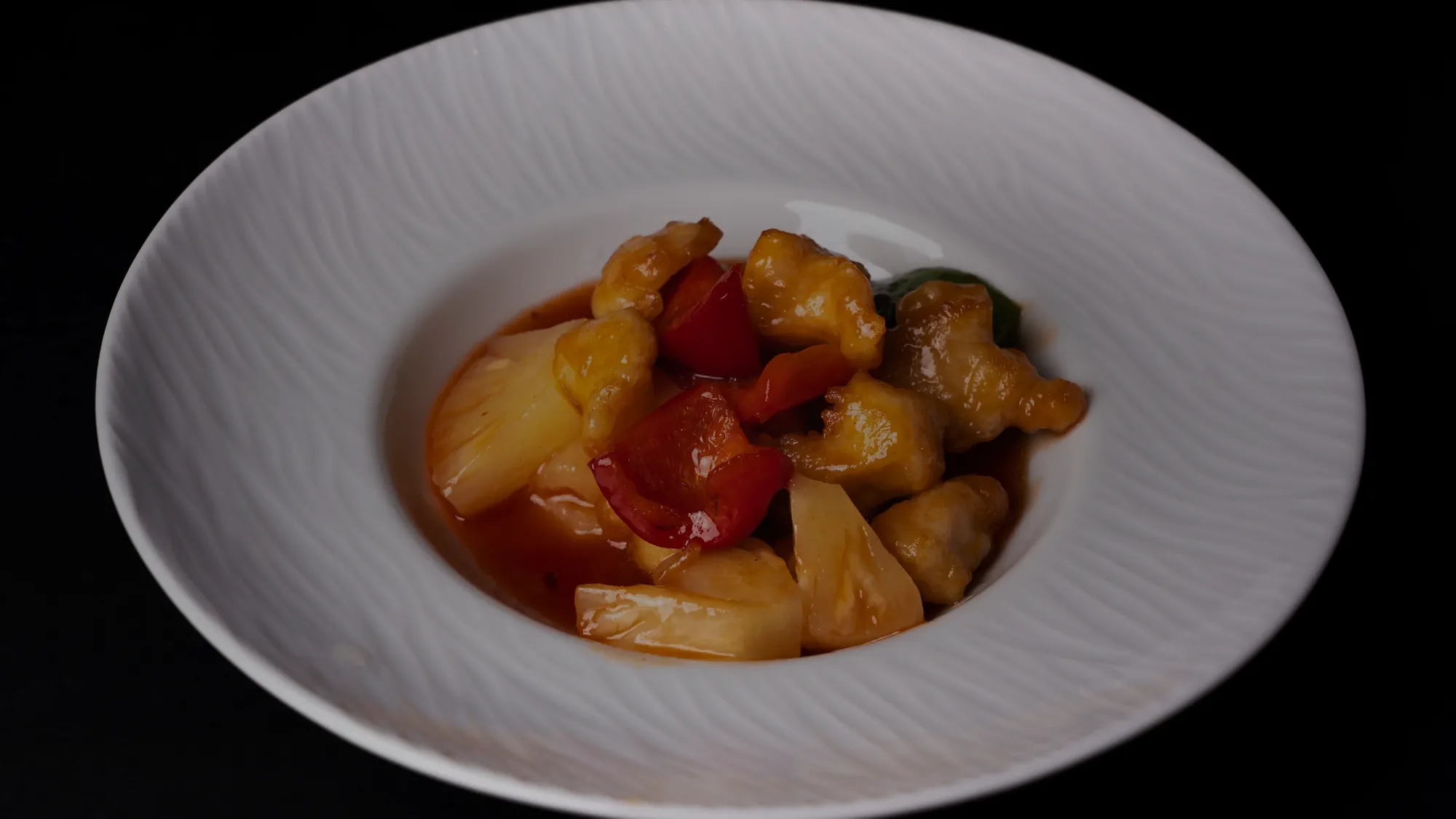 Poulet frit nappé de sauce aigre-douce avec ananas et poivron rouge dans une assiette creuse blanche